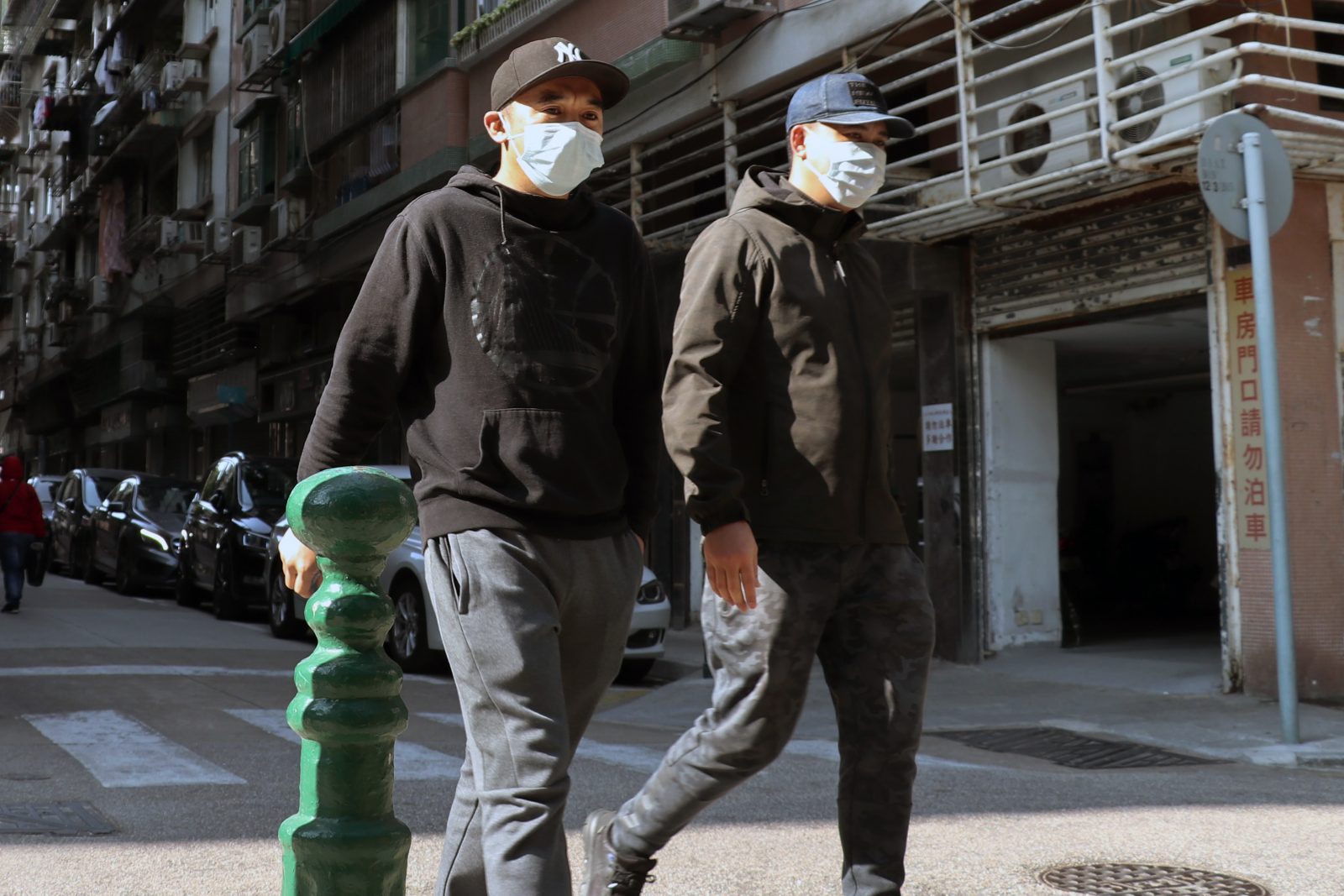 Duas pessoas agasalhadas andando lado a lado na rua com máscaras faciais.